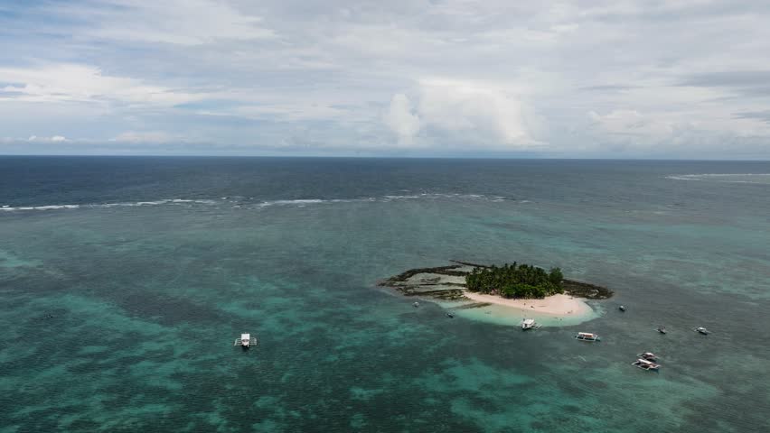 Tourist boats anchored close to a sandy tropical island with palm trees. Guyam Island. Siargao, Philippines.