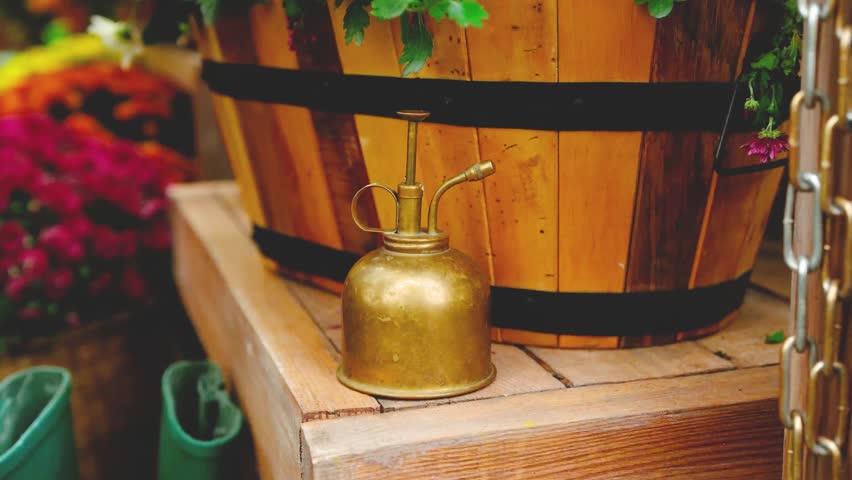 Antique golden mister spray bottle sits on rustic wooden planks near a large wooden barrel