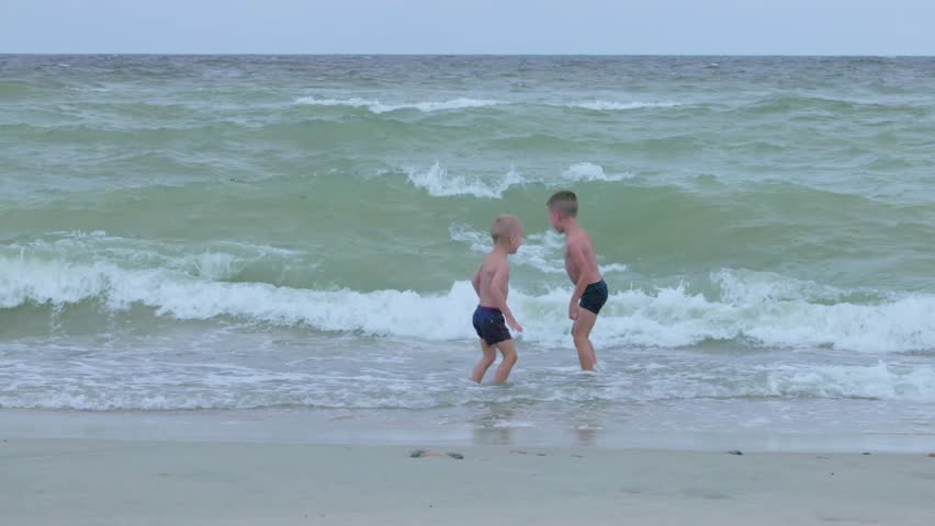 Two kids are having a great time at the beach, joyfully playing in the surf and embracing the waves