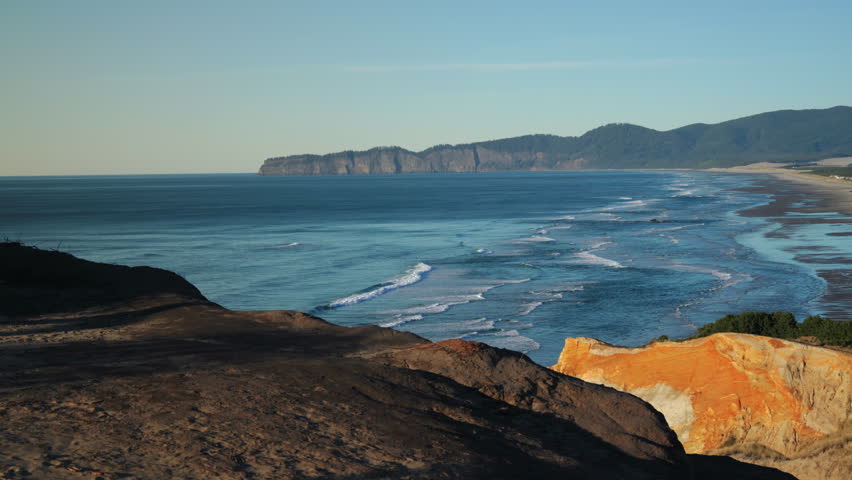 Wide coastal view of Oregon Coast with rocky cliffs, rolling Pacific Ocean waves, textured shoreline, natural light, layered landscape and open horizon.