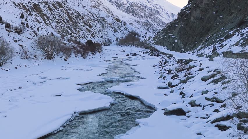 Icy Flow: A Partially Frozen Mountain Stream Winding through a Pristine Snow-Blanketed Alpine Valley.