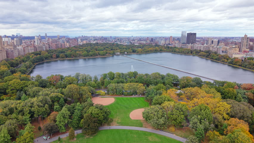 Top aerial view of Central Park showing green lawns, walking paths and dense trees, large urban park with baseball fields surrounded by Manhattan buildings in New York City environment