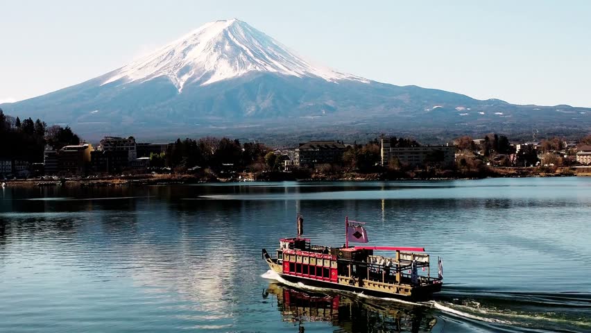 Aerial drone view on 9 November 2025 of Mount Fuji rising above Fujikawaguchiko town, Japan, showing Lake Kawaguchi, traditional houses, autumn scenery, clear sky, and peaceful landscape, capturing iconic Japanese nature, travel beauty, and cultural atmosphere.