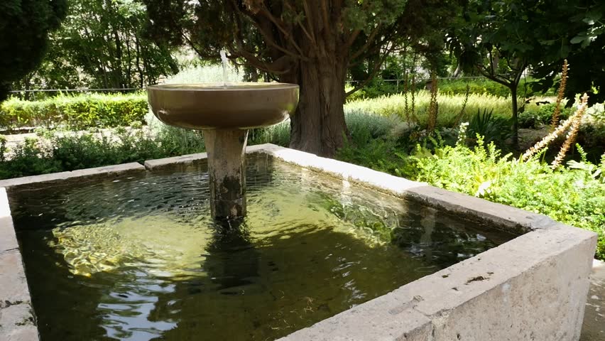 Traditional stone fountain with water flowing into a square pond, surrounded by the lush vegetation of the Nasrid Garden in Vélez de Benaudalla.