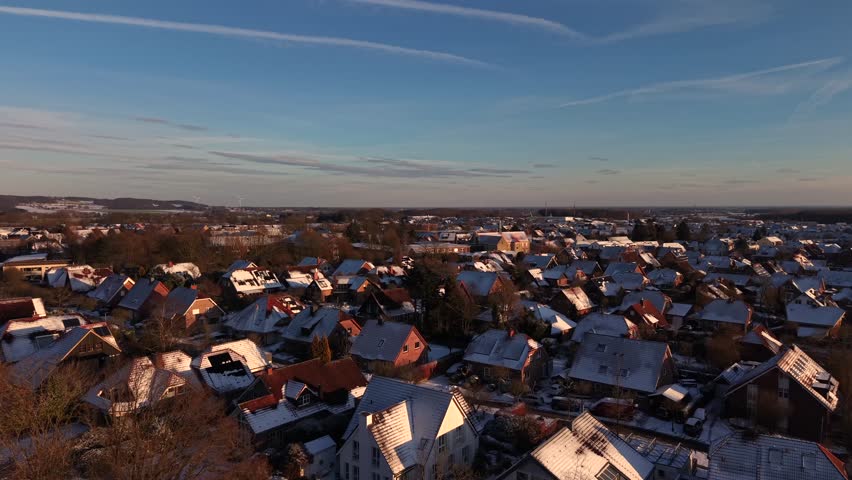 Snow-covered orange roofs of red brick houses on snowy winter day in Germany. Aerial forward wide shot. Peaceful and quiet suburbia at sunset with blue sky. Single family houses in Germany.