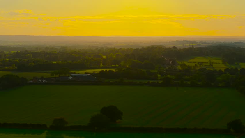 Golden light covering green agricultural valley during calm sunset. Soft rays illuminating farmland and distant hills. Peaceful countryside shining under warm evening glow