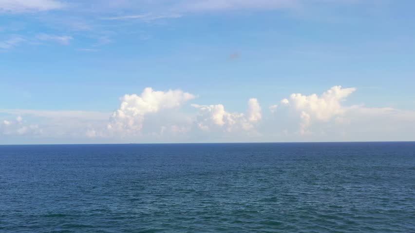 Aerial view of calm ocean water with fluffy clouds on the horizon. Perfect concept for travel, relaxation, tourism, promo, and nature backgrounds. High quality, scenic footage.