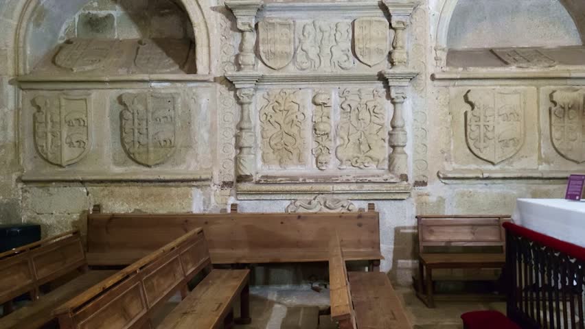 Tombs and Heraldic shields carved in stone. Medieval symbols. Panoramic view of a wall with feudal tombs and shields carved in stone and a stained-glass window with vibrant colors.