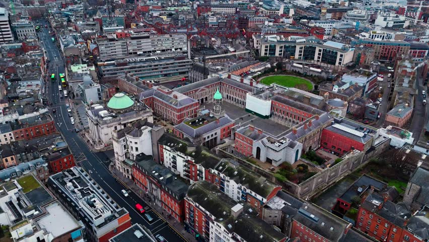 Drone shot over Dublin castle in the city centre in Ireland with busy streets below with cars and buses and tourists walking around in Irish cityscape on cloudy overcast day in winter