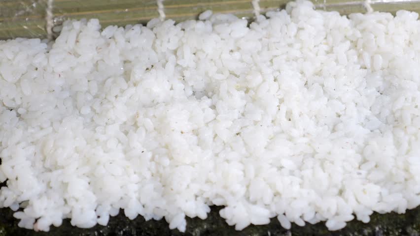 A gloved sushi chef sprinkles sesame seeds on rice while making sushi. Japanese cuisine, Asian cuisine close-up. Takeaways, food delivery.