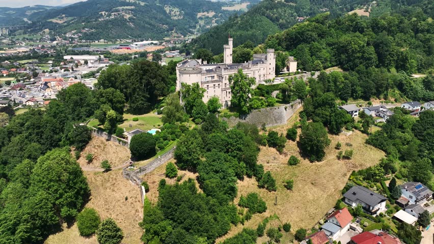 Aerial summer footage of Wolfsberg showing town center, church towers, green hills, layered valleys, warm light, smooth drone flight, atmospheric European small-town scenery