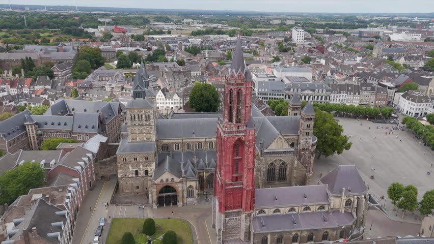 High-altitude drone footage of the historic city center of Maastricht, showcasing the iconic red tower of Saint John’s Church next to the Basilica of Saint Servatius at the Vrijthof square, surrounded