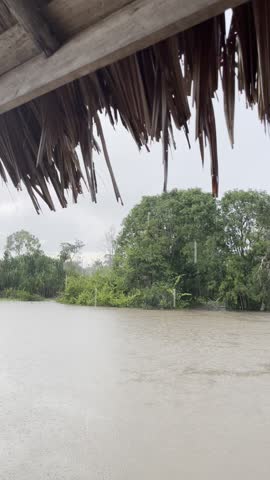 Rain falling over a small hut with a leaf roof located in the middle of a river, creating a calm and atmospheric rural scene