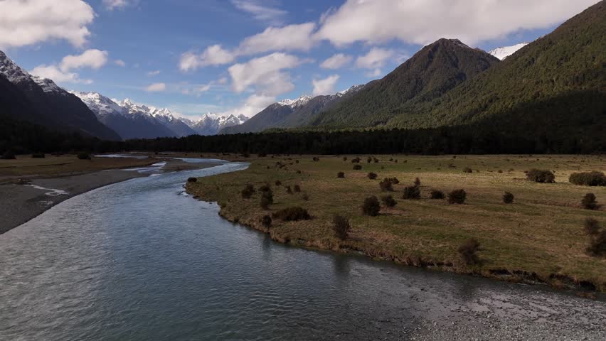 Cinematic low-altitude drone shot of a clear mountain creek flowing between snow-capped peaks in Southland, New Zealand, on the way to Milford Sound at 4K 60fps