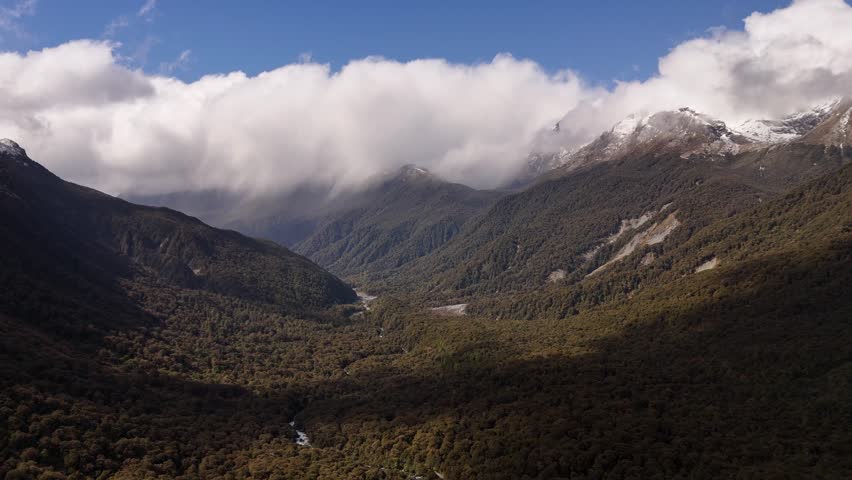 Dramatic drone footage of misty clouds rolling over the peaks of the Southern Alps along the scenic road to Milford Sound in Southland, New Zealand