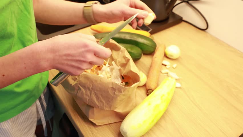 Hands peeling garlic with a knife during food preparation on a kitchen table. Fresh vegetables and home cooking process.