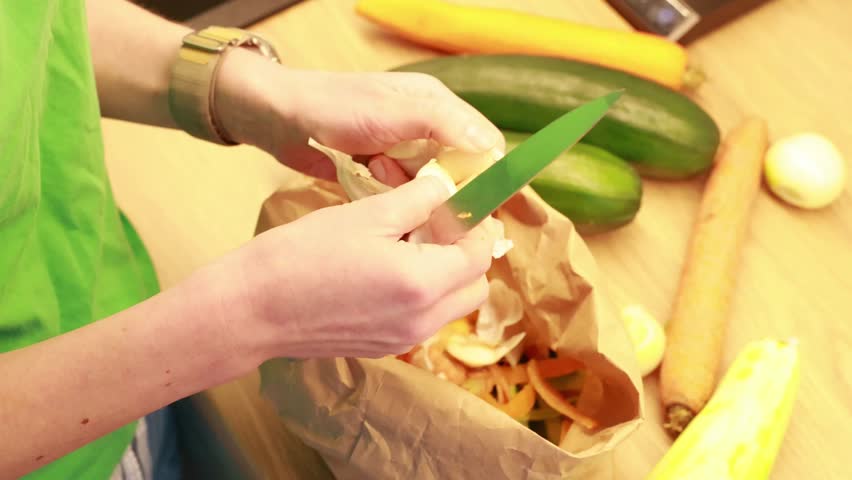 Hands peeling garlic with a knife during food preparation on a kitchen table. Fresh vegetables and home cooking process.