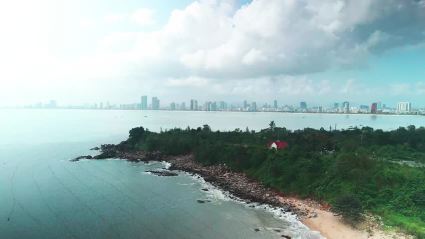 Da nang cityscape stretching along the bay, framed by the lush son tra peninsula coastline with a small white house and rocky beach, presenting a vibrant urban and natural landscape
