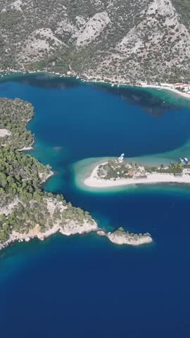 An elevated perspective showcases a striking natural landscape with a vibrant blue sea meeting a sandy spit and verdant, rocky slopes