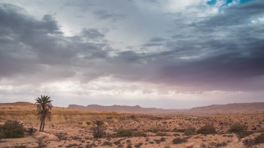 Timelapse: dramatic cloudy sky in Dahar mountains desert landscape in southern Tunisia, arid plateau with palm trees, remote wilderness, Sahara fringe, travel destination, North Africa