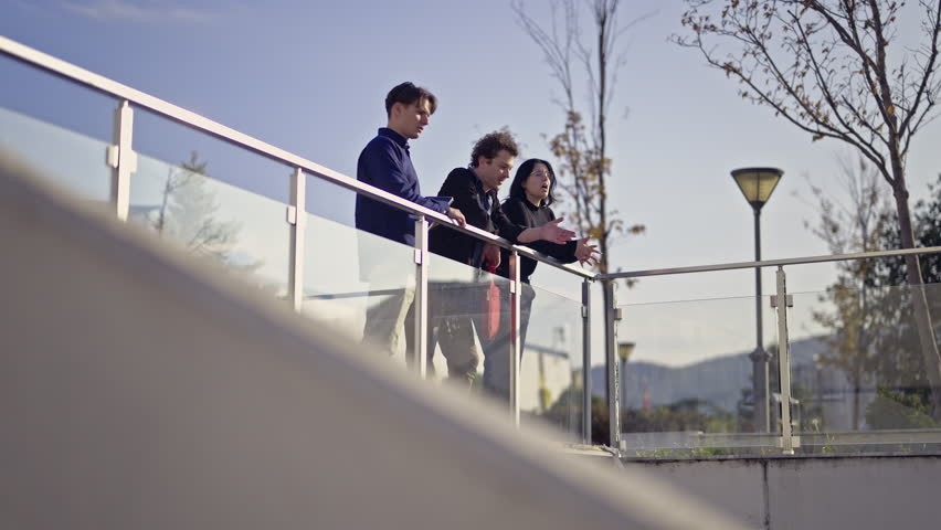 Engaged business people collaborate on a contemporary outdoor terrace, exchanging ideas and observations. Their focused discussion reflects teamwork and strategic planning in a bright environment.