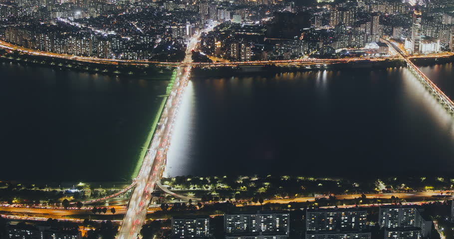 A nighttime view of a bustling city with illuminated bridges and flowing traffic over a river, highlighting urban vibrancy and movement. Time-lapse, Seoul, South Korea