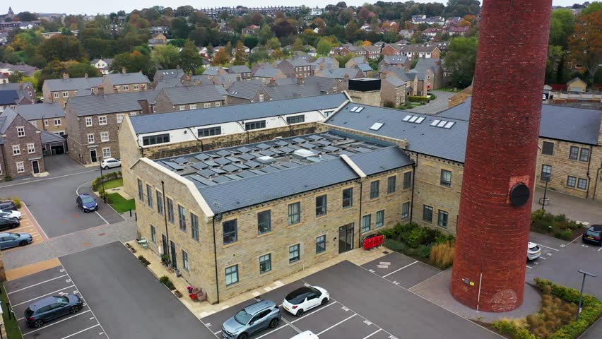 Aerial drone footage of the town of Yeadon in Leeds West Yorkshire UK Showing a brand new housing estate with rows of houses next to an old converted industrial mill buildings and original chimney 