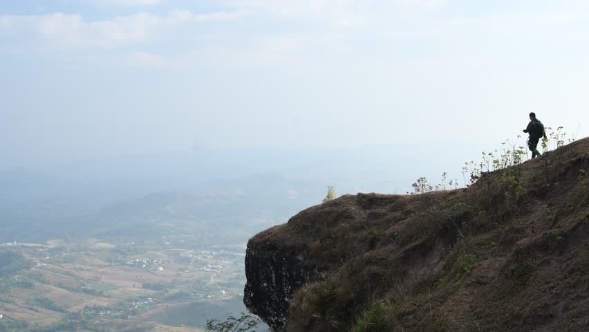 Adventurous man is standing on top of the mountain and enjoying the beautiful view during a vibrant.
