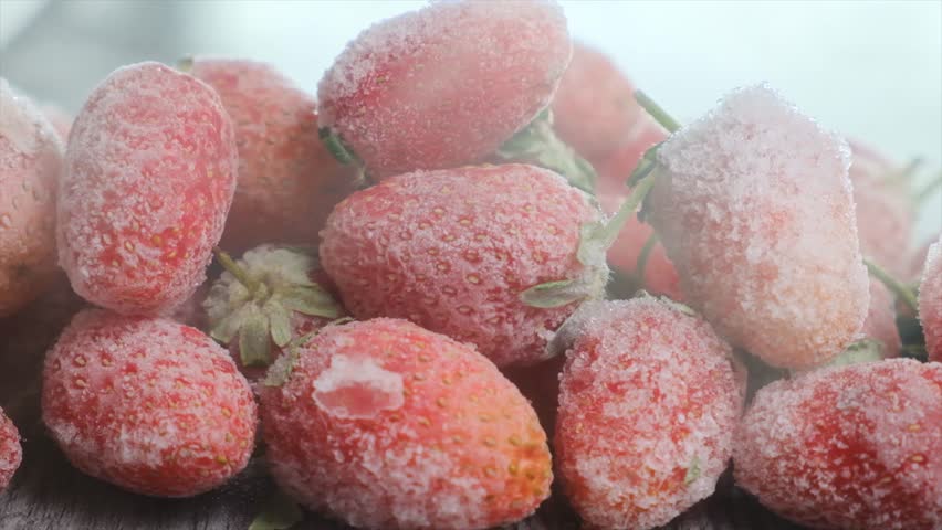 Close up pile of large strawberry berries intensely frozen by a stream of cold air and covered with frost. Fast freezing of berries preserves useful properties. Dry freezing. Freezing technology.
