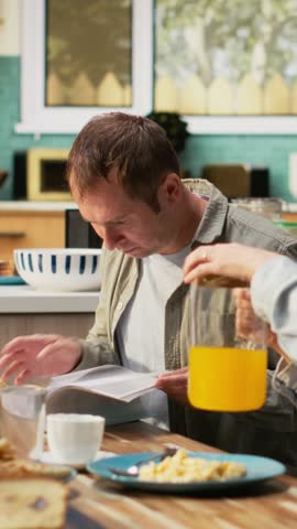Vertical Video Preoccupied working dad studying work reports and documents at breakfast, ignoring his pre-teen girl and wife during family time. Father focused on papers, neglecting his daughter