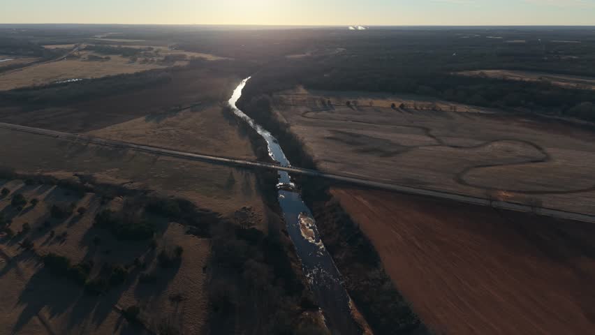 Aerial view of a winding river reflecting sunlight as it flows through rural Oklahoma farmland during winter.