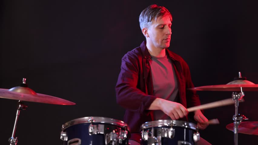Man playing drums with drumsticks in color light against black background