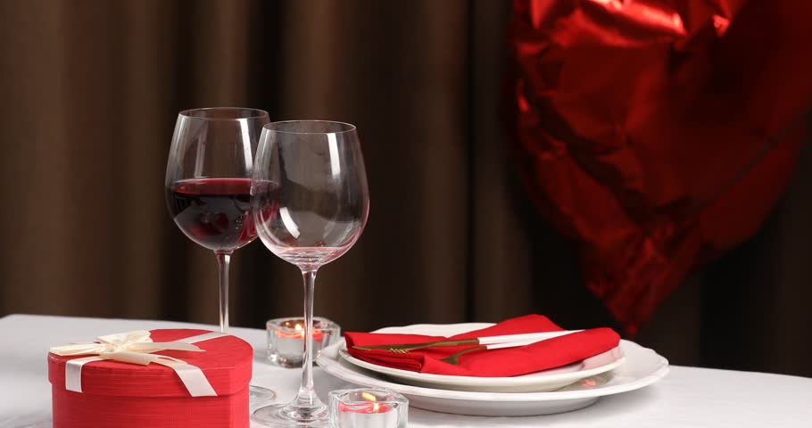 Woman pouring red wine into glass at white table indoors, closeup