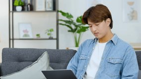 Frustrated young man in a denim shirt uses a laptop while sitting on the sofa - Powered by Shutterstock - Get 15% off with code: PIKWIZARD15