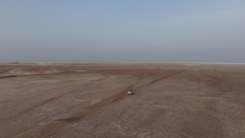 Aerial push-in shot following a white off-road vehicle driving across the desolate salt flats of Ethiopia