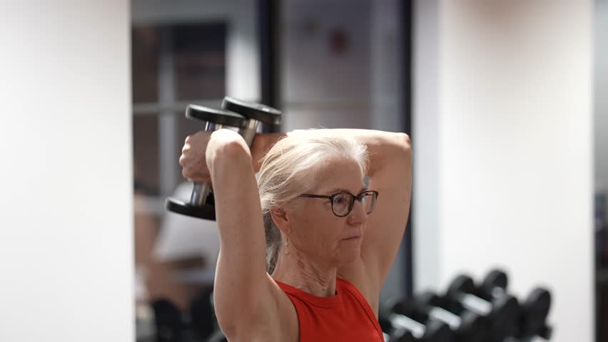 Mature woman works out in gym, lifting weights to build strength and improve health during her fitness routine.
