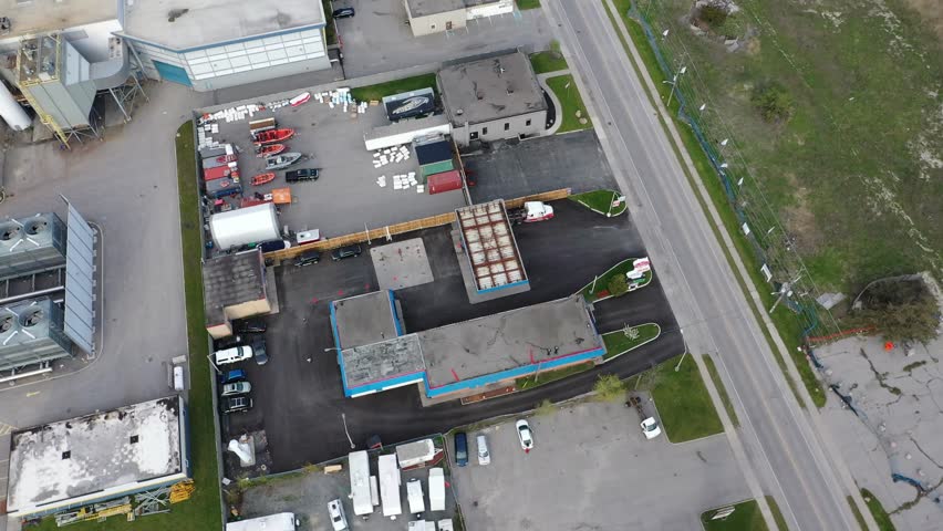 High angle drone view circling an industrial commercial district with warehouses, parking lots, and various vehicles including trucks and boats. In ajax ontario canada