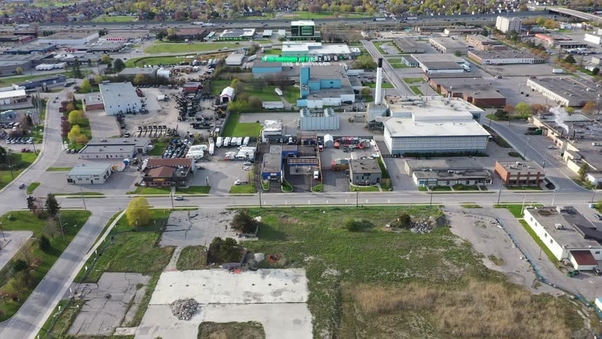 Aerial view flying over a commercial and industrial district with warehouses, factories, and commercial buildings under a clear sky. In ajax ontario canada