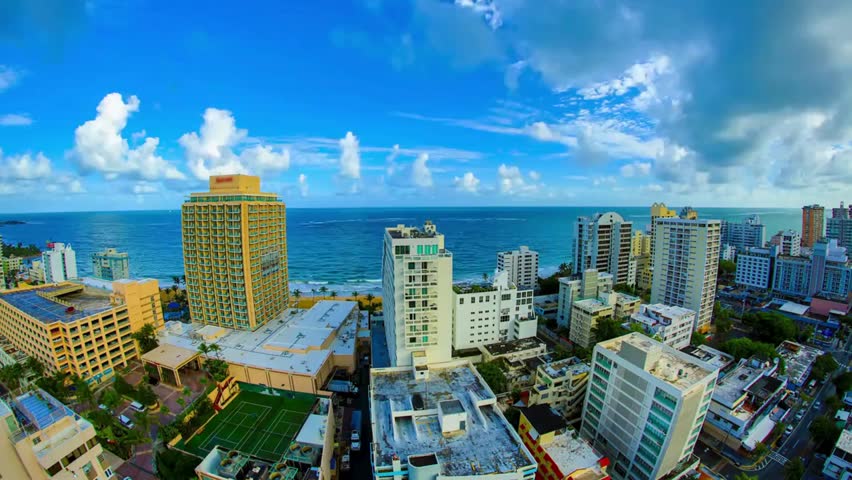 Panoramic view of San Juan, Puerto Rico skyline along the coastline, featuring modern buildings, blue ocean water and a sunny tropical vibe.