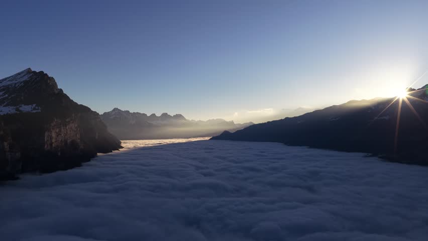 Aerial sunset over Lake Walensee in the Swiss Alps, with sea of clouds filling the valley and warm sun rays glowing on mountain peaks.