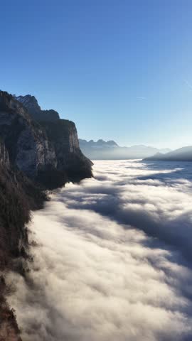 Vertical view of a mountain cliff rising above a sea of clouds. Drone 4k.