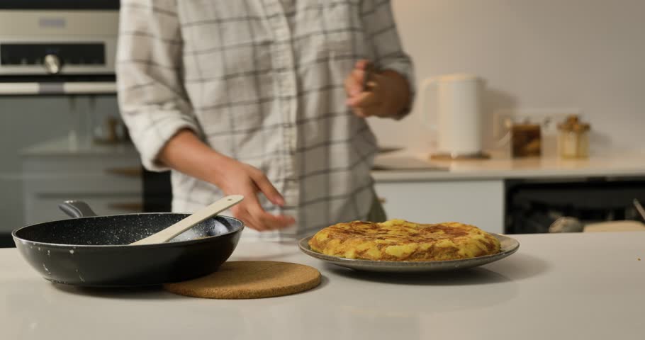 Woman cutting Spanish omelette on plate in modern kitchen