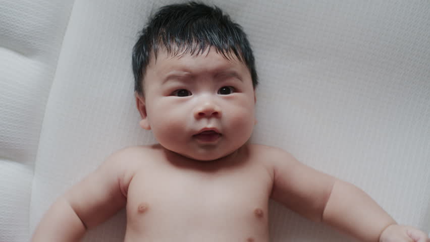 Newborn baby asian boy  laughs lying on the bed.