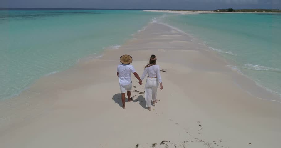 Couple holding hands walking on the white sandbar of Cayo de Agua, Los Roques Archipelago, Venezuela, with turquoise Caribbean waters.