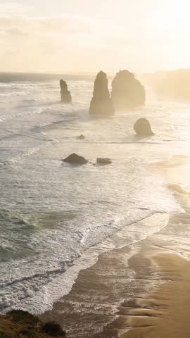 A golden sunset illuminates limestone stacks and crashing waves along a scenic vertical coastline.