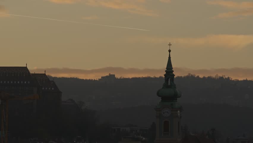 Church Tower With Clock Against Foggy Hills And Dusk Sky In Budapest, Hungary. static shot