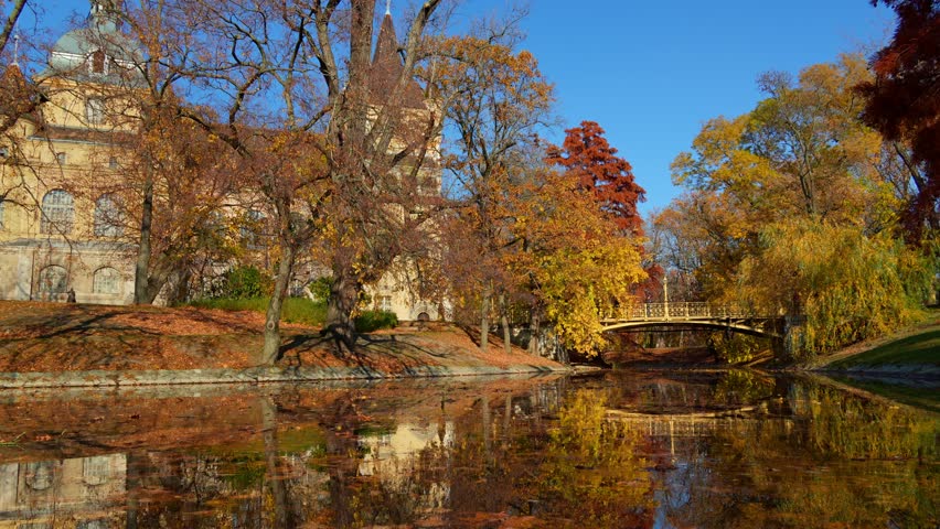 City park on bright autumn day, decorative foot bridge over pond, yellow and golden autumn leaves on trees, beautiful nature in Varosliget park near Vajdahunyad Castle, Budapest, Hungary