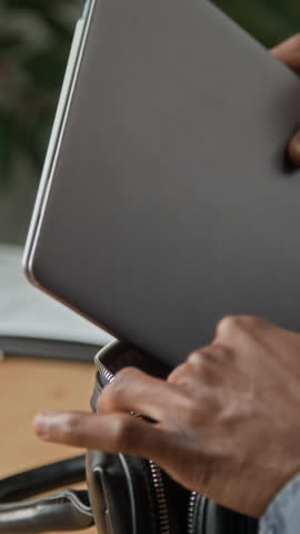 Vertical rear view of young African American businessman opening window blinds and looking outside with sunlight entering modern office creating reflective and thoughtful atmosphere