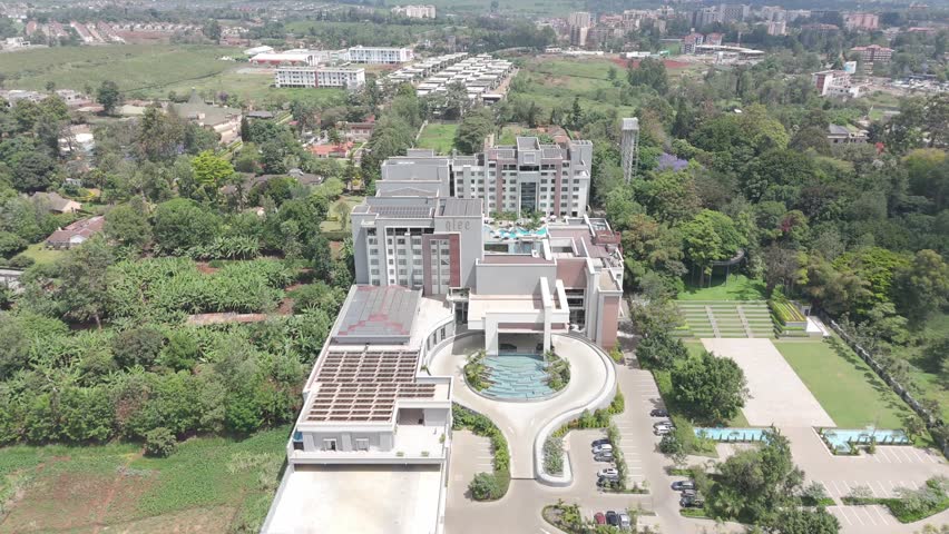 Daytime aerial zoom in over Hotel Glee Nairobi showing modern architecture, surrounding greenery and urban development.