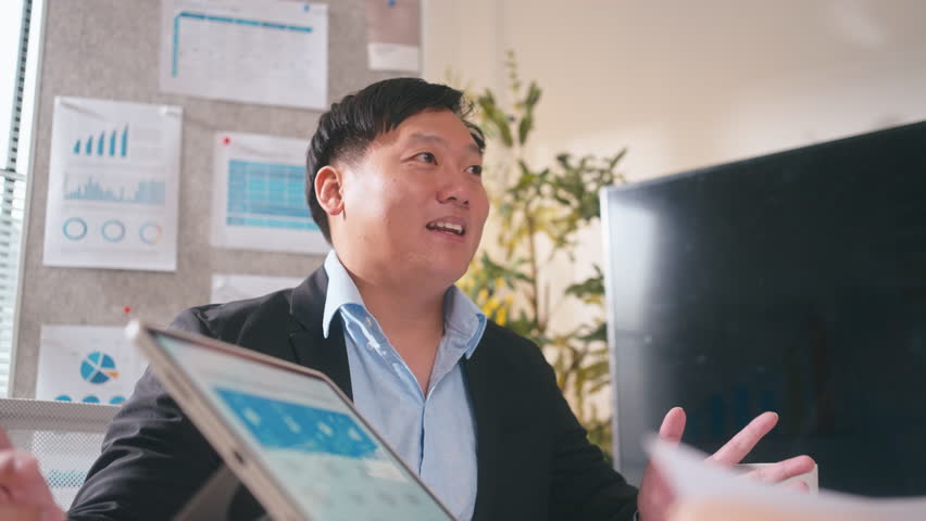 Group of Asian professionals reviewing business statistics and reports together in office.